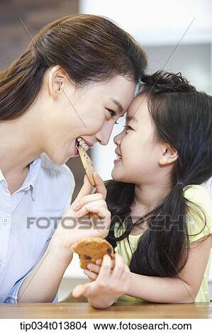 Picture - a mother and a daughter enjoying cookies in the kitchen. Fotosearch