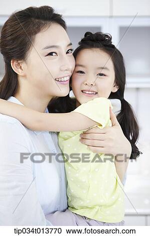 Stock Image - a mother and a daughter hugging in the kitchen. Fotosearch