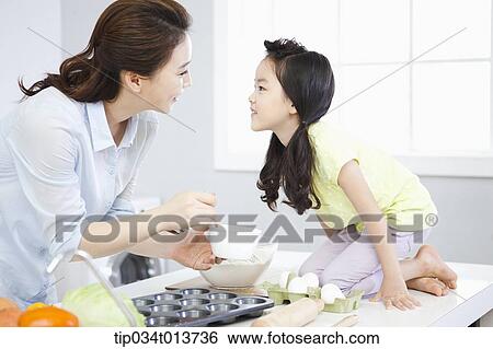Stock Photograph - a mother and a daughter looking at each other in the kitchen. Fotosearch