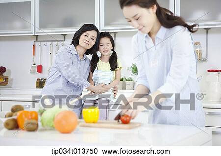 Stock Image - a mother and a daughter watching a woman cooking. Fotosearch