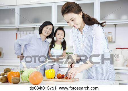 Stock Image - a mother and a daughter watching a woman cooking. Fotosearch