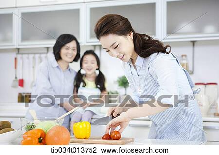 Stock Image - a mother and a daughter watching a woman cooking. Fotosearch