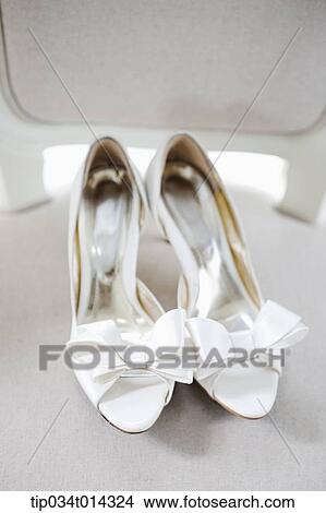 Picture - a pair of white heels with ribbon on a chair. Fotosearch