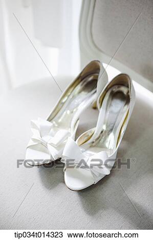 Stock Image - a pair of white heels with ribbon on a chair. Fotosearch