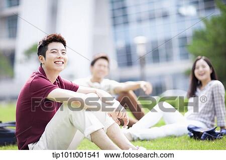 Stock Image - a student sitting on grass with students talking in background. Fotosearch