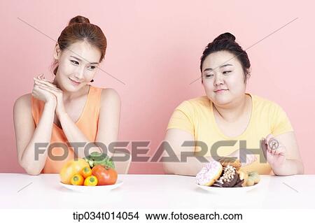Picture - a thin and chubby woman sitting at table with different food in front. Fotosearch