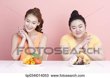 Stock Image - a thin and chubby woman sitting at table with different food in front. Fotosearch