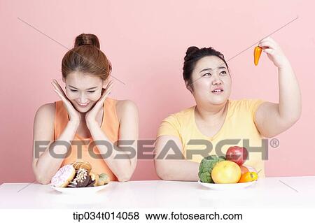 Stock Photo - a thin and chubby woman sitting at table with different food in front. Fotosearch