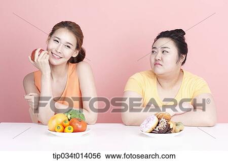Stock Photograph - a thin and chubby woman sitting at table with different food in front. Fotosearch