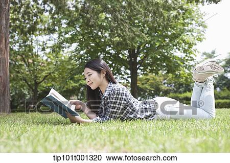 Stock Image - a university student lying on grass reading a book. Fotosearch