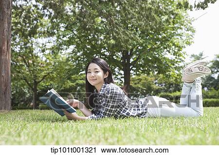 Stock Image - a university student lying on grass reading a book. Fotosearch