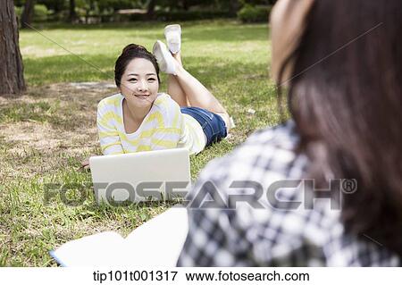 Stock Photo - a university student lying on grass using laptop. Fotosearch