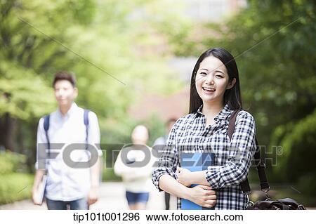 Stock Photograph - a university student standing in the campus holding books. Fotosearch