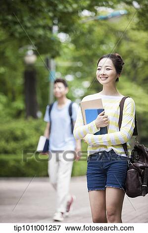 Stock Photo - a university student walking in the campus holding books. Fotosearch