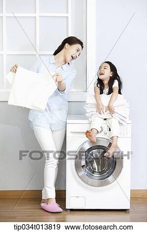 Stock Photo - a woman and a daughter playing around washing machine. Fotosearch