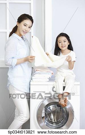 Stock Image - a woman and a daughter posing at washing machine. Fotosearch