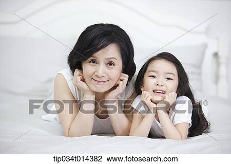 Stock Image - a woman and granddaughter lying on a bed. Fotosearch