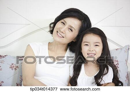 Stock Photo - a woman and granddaughter posing while sitting on a bed. Fotosearch