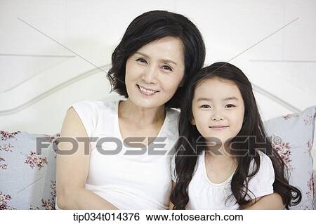 Stock Photograph - a woman and granddaughter posing while sitting on a bed. Fotosearch