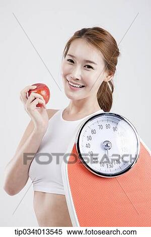 a woman holding a weighing scale and an apple View Large Photo Image Stock Photography - a woman holding a weighing scale and an apple. Fotosearch