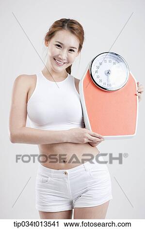 Stock Image - a woman holding a weighing scale. Fotosearch