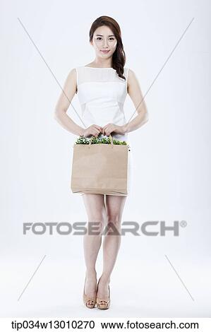 Stock Image - a woman in a white dress holding a bag full of plants. Fotosearch