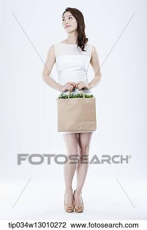 Stock Image - a woman in a white dress holding a bag full of plants. Fotosearch