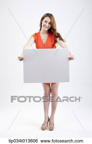 Stock Photograph - a woman in orange dress posing with an empty white board. Fotosearch