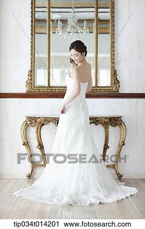 Stock Image - a woman in wedding dress standing in front of mirror . Fotosearch
