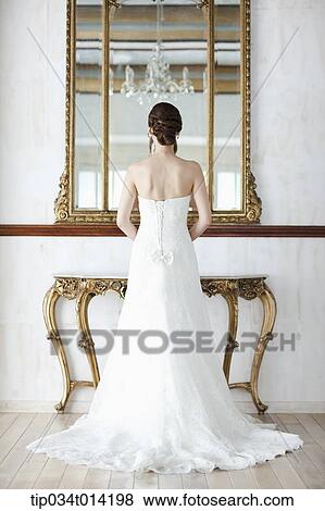 Stock Photo - a woman in wedding dress standing in front of mirror . Fotosearch