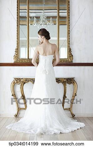 Stock Photo - a woman in wedding dress standing in front of mirror . Fotosearch