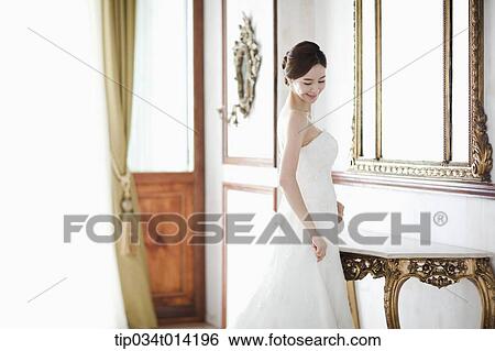 Stock Photograph - a woman in wedding dress standing in front of mirror . Fotosearch