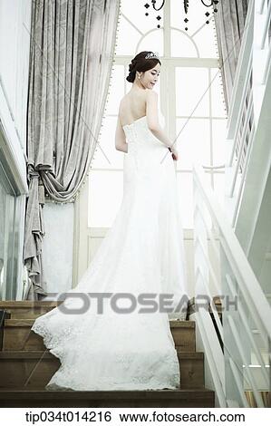Stock Photograph - a woman in wedding dress standing on the stairs looking back. Fotosearch