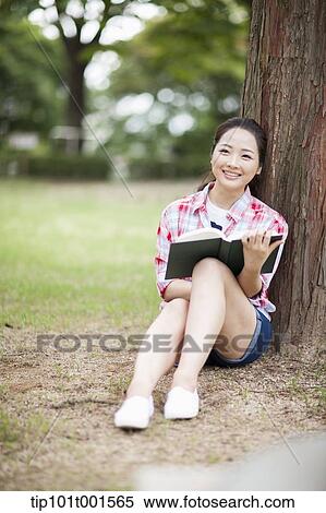 Stock Photography - a woman leaning on tree reading a book. Fotosearch
