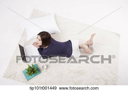 Stock Photo - a woman lying on a carpet using laptop. Fotosearch