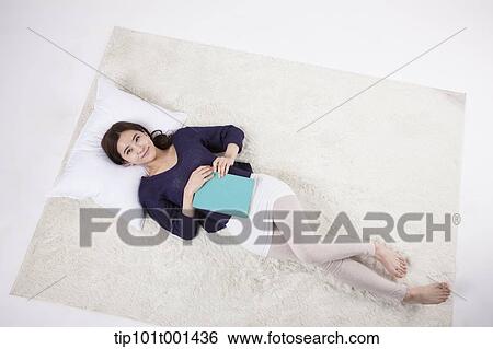 Stock Photograph - a woman lying on a pillow holding a book. Fotosearch