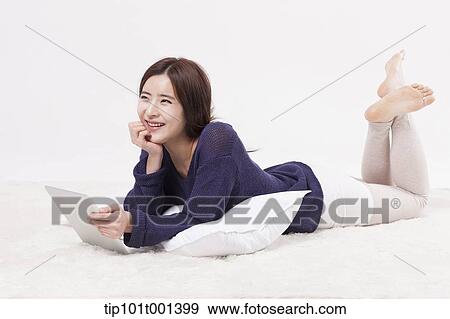 Stock Photo - a woman lying on a pillow using tablet PC. Fotosearch