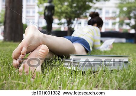 Stock Image - a woman lying on grass next to books . Fotosearch