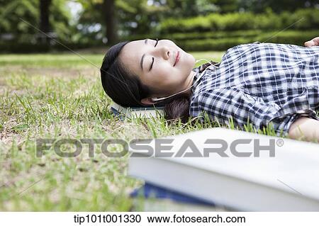 Stock Image - a woman lying on grass with eyes closed. Fotosearch