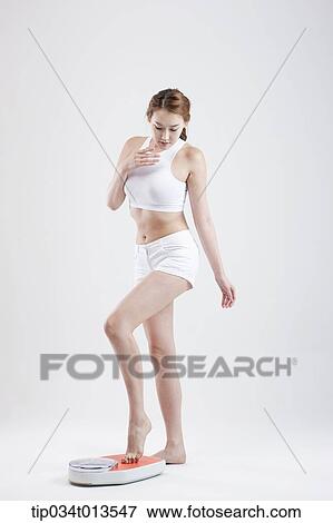 Stock Photo - a woman measuring herself on weighing scale. Fotosearch