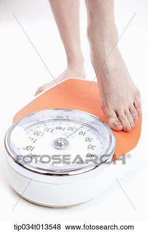 Stock Photo - a woman measuring herself on weighing scale. Fotosearch