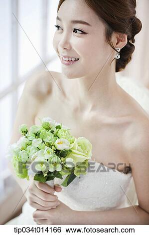 Stock Photograph - a woman posing with wedding dress and flower bouquet. Fotosearch