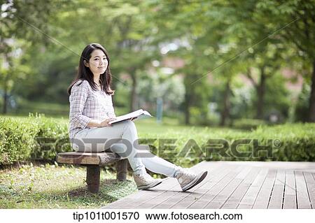 Stock Image - a woman sitting on a bench reading a book. Fotosearch