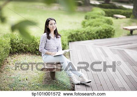 Stock Image - a woman sitting on a bench reading a book. Fotosearch