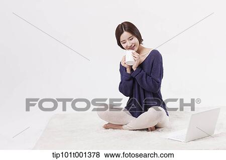 Stock Photo - a woman sitting on a carpet holding a coffee cup. Fotosearch
