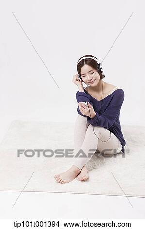 Picture - a woman sitting on a carpet listening to a music . Fotosearch