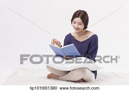 Stock Image - a woman sitting on a carpet reading a book. Fotosearch