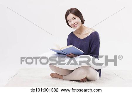 Stock Image - a woman sitting on a carpet reading a book. Fotosearch
