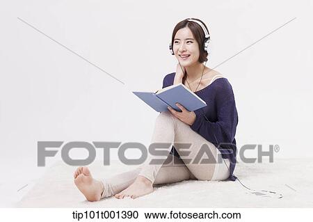 Stock Image - a woman sitting on a carpet reading a book listening to a music . Fotosearch