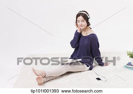 Stock Image - a woman sitting on a carpet reading a book listening to a music . Fotosearch